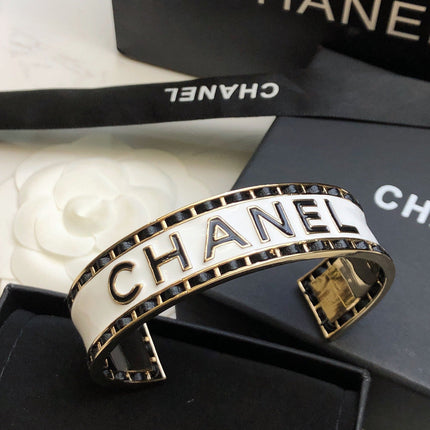 CHANEL 26S CHANEL LOGO ENAMEL CUFF BRACELET WITH BLACK TRIM IN GOLD METAL 630835