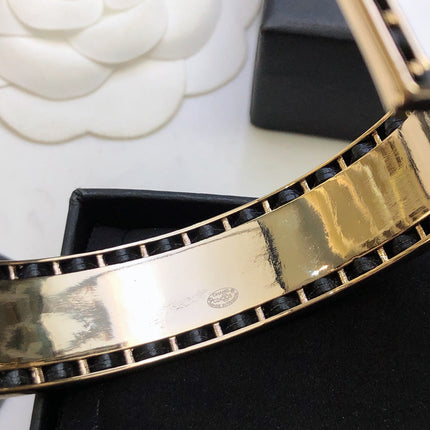 CHANEL 26S CHANEL LOGO ENAMEL CUFF BRACELET WITH BLACK TRIM IN GOLD METAL 630835