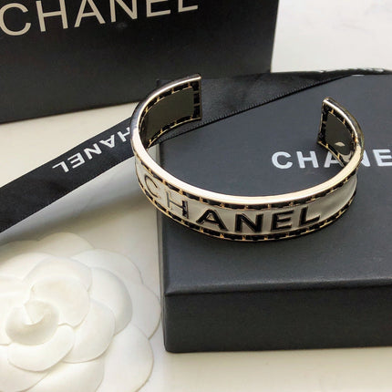 CHANEL 26S CHANEL LOGO ENAMEL CUFF BRACELET WITH BLACK TRIM IN GOLD METAL 630835