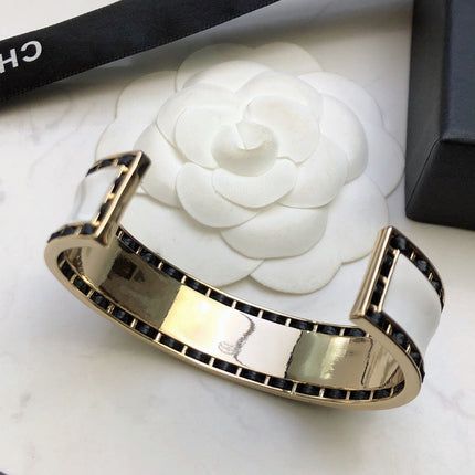 CHANEL 26S CHANEL LOGO ENAMEL CUFF BRACELET WITH BLACK TRIM IN GOLD METAL 630835